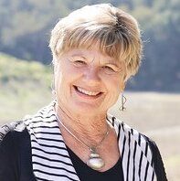 Woman with blonde hair smiling, wearing a striped scarf and necklace, outdoors.