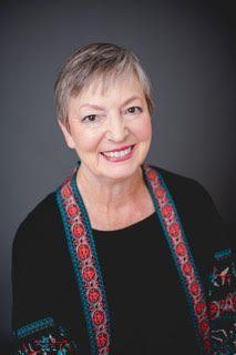 Woman with short hair smiles, wearing black top with colorful trim, against gray background.