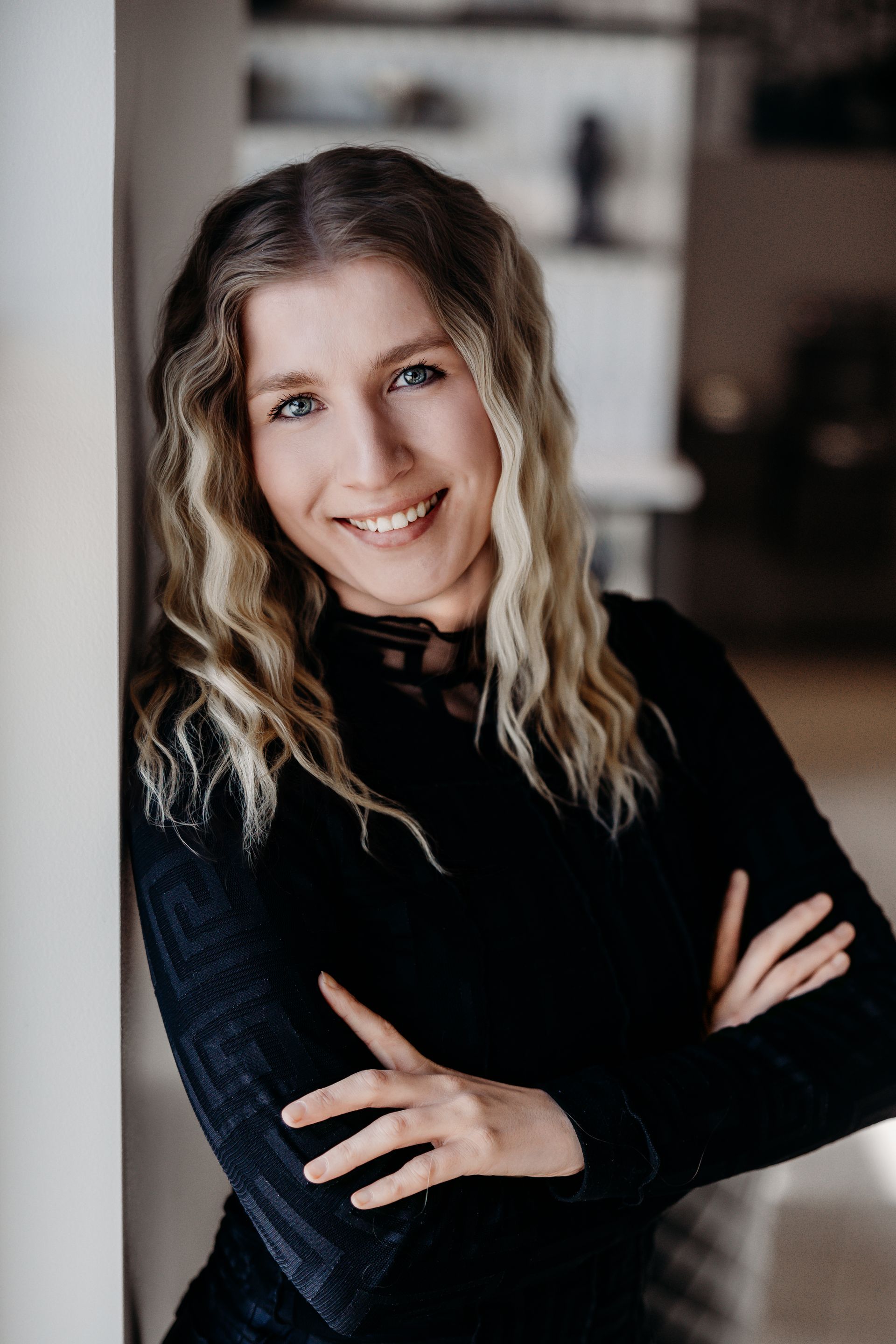 A woman is leaning against a wall with her arms crossed and smiling.