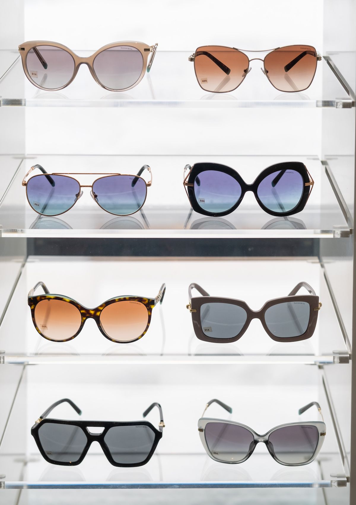 A variety of sunglasses are displayed on a shelf in a store.