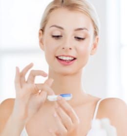 A woman is holding a pair of contact lenses in her hand.