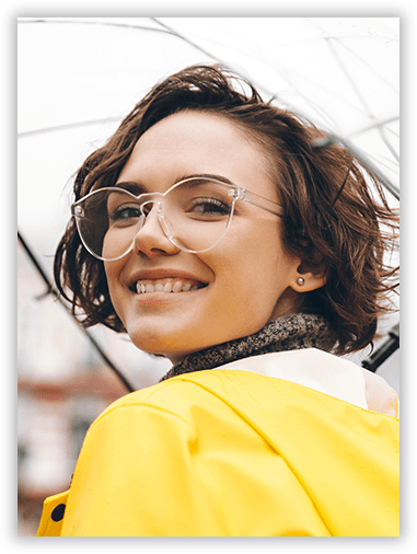 A woman wearing glasses and a yellow raincoat is smiling while holding an umbrella.