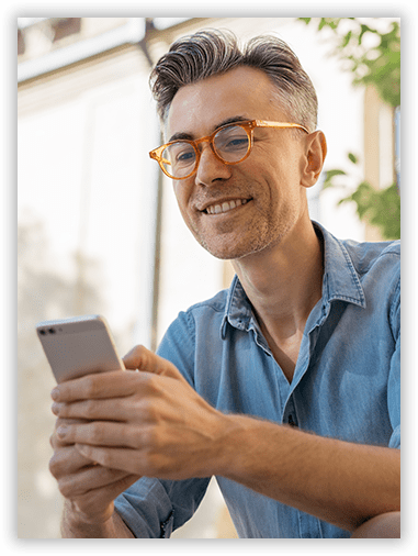 A man wearing glasses is smiling while looking at his cell phone.