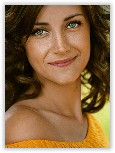 A close up of a woman 's face with green eyes wearing a yellow sweater.