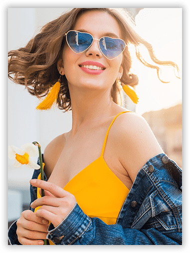 A woman wearing sunglasses and a yellow dress is holding a flower.