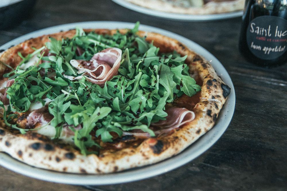 A pizza on a plate with a bottle of wine in the background.