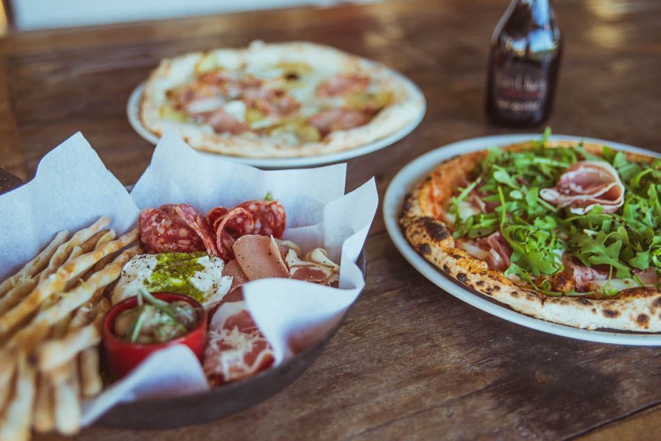 A wooden table topped with three plates of pizza and french fries.