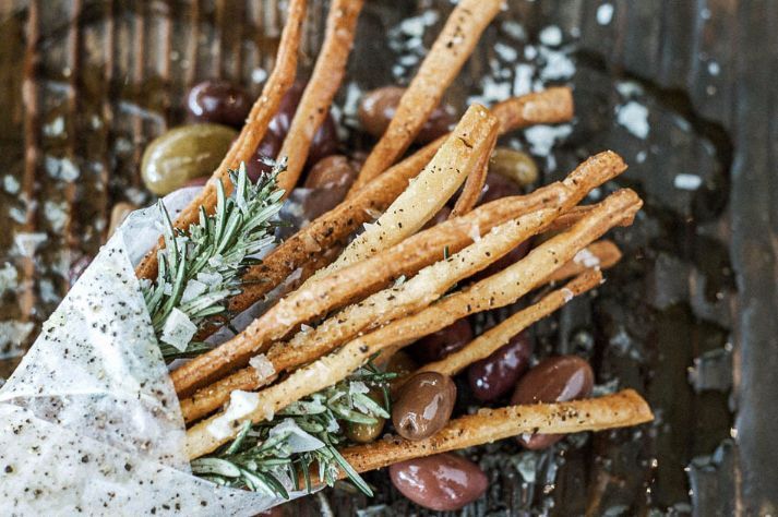 A close up of a bag filled with bread sticks and olives.