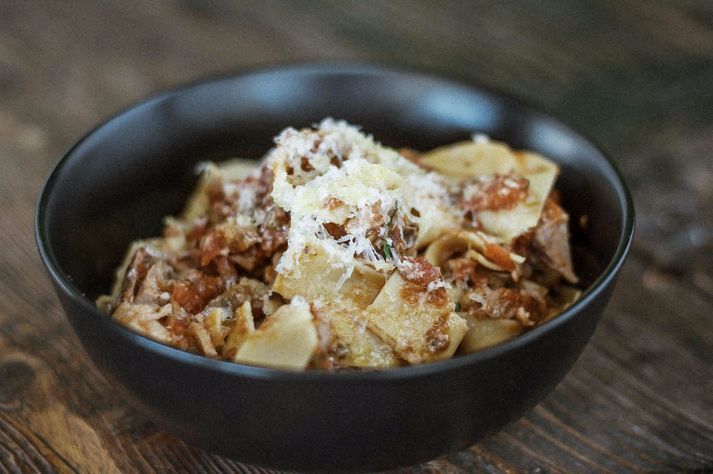 A bowl of pasta with meat and cheese on a wooden table.