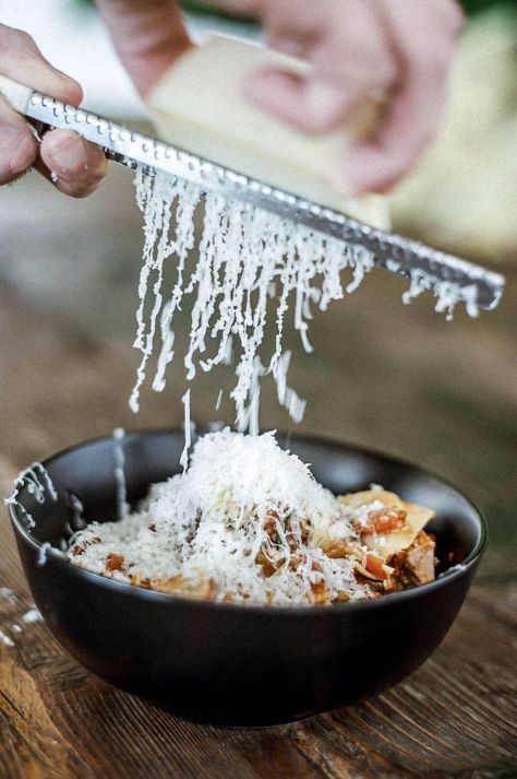 A person grating cheese over a bowl of pasta