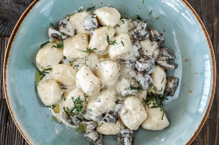 A bowl of gnocchi with mushrooms and sauce on a wooden table.