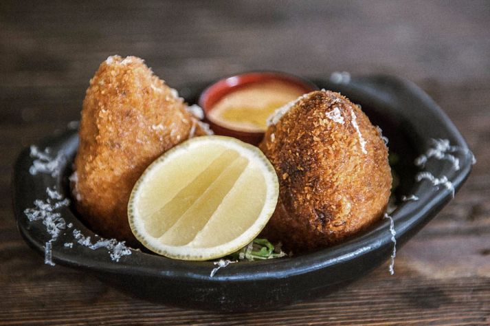 A black bowl filled with fried food and a slice of lemon.