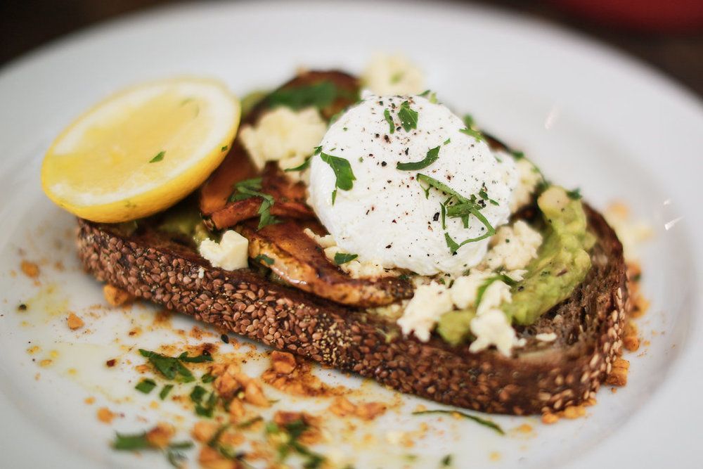 A close up of a plate of food with avocado , lemon , and poached egg.