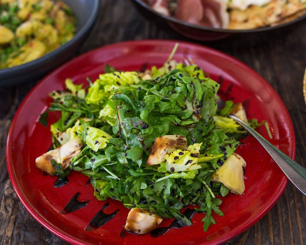 A red plate topped with a salad and a fork on a wooden table.