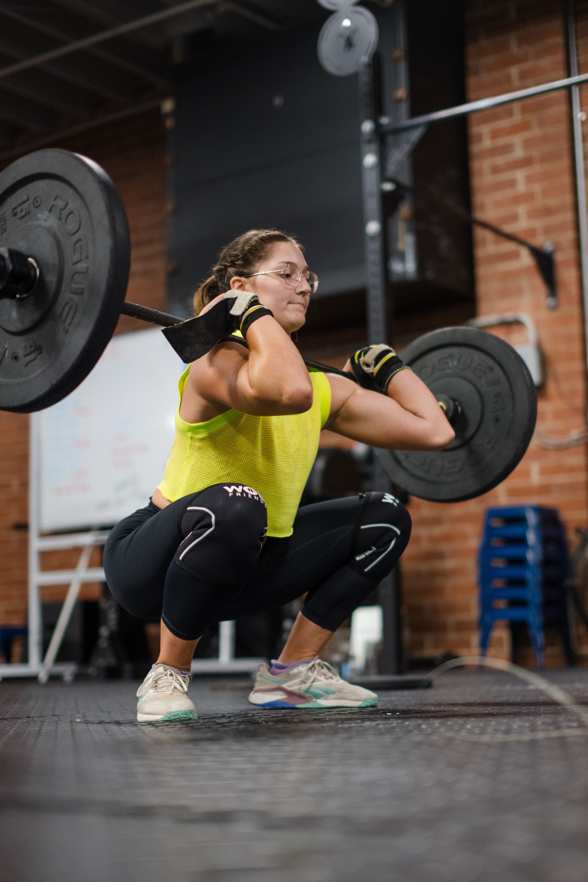 A woman is squatting with a barbell over her head in a gym.