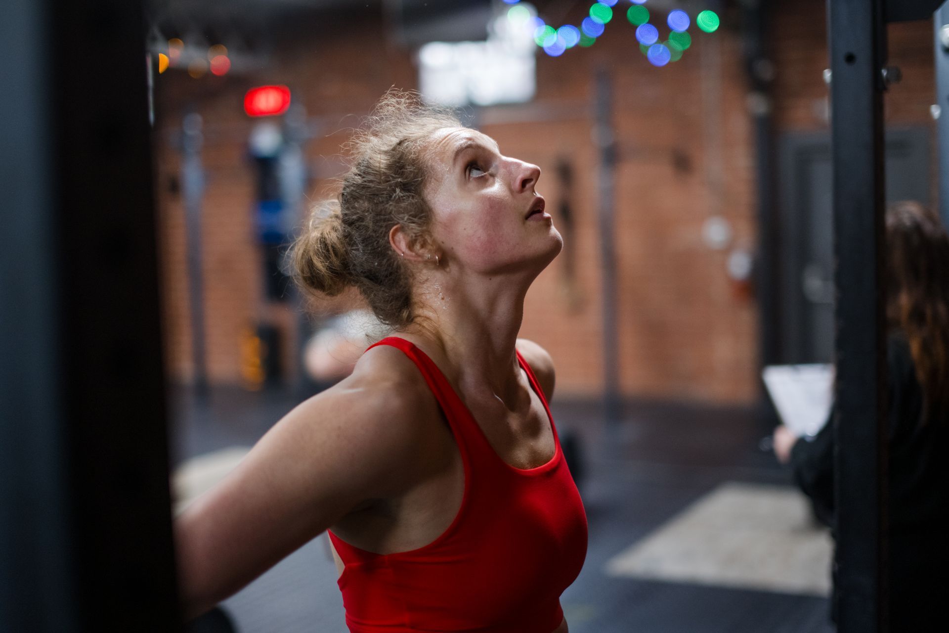 A woman in a red tank top is looking up in a gym.