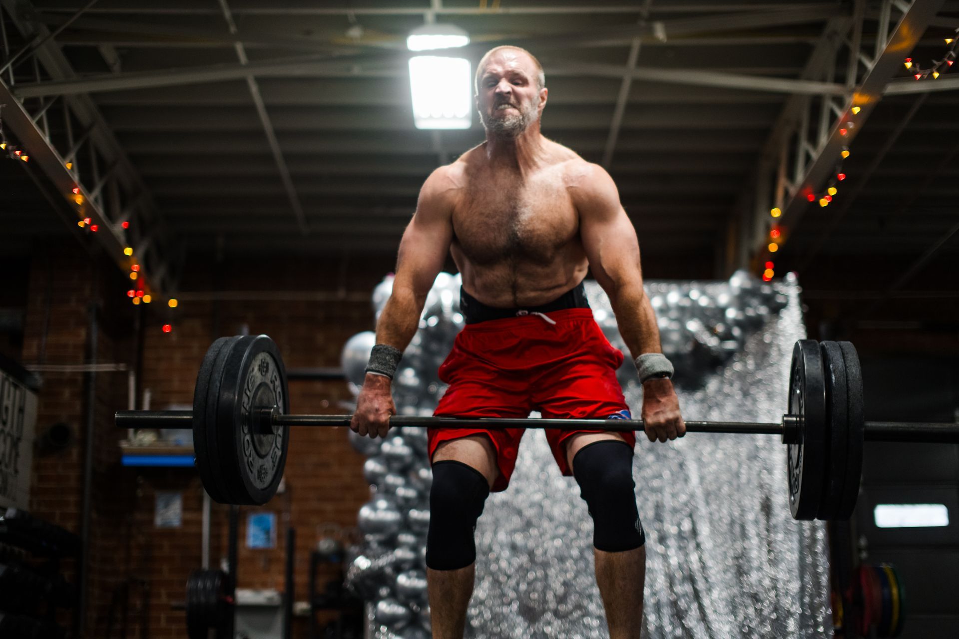 A shirtless man is lifting a barbell in a gym.