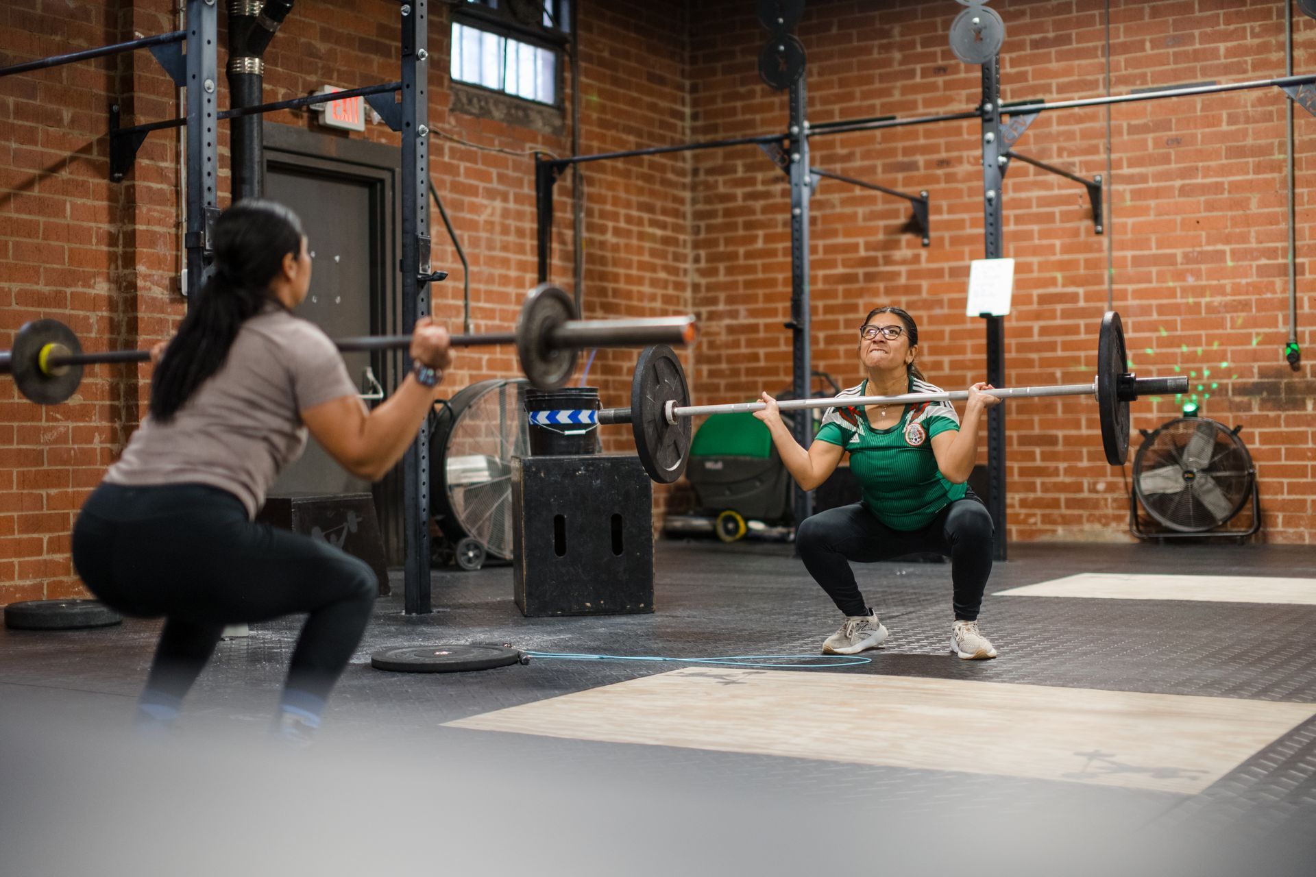 Two women are squatting with a barbell in a gym.
