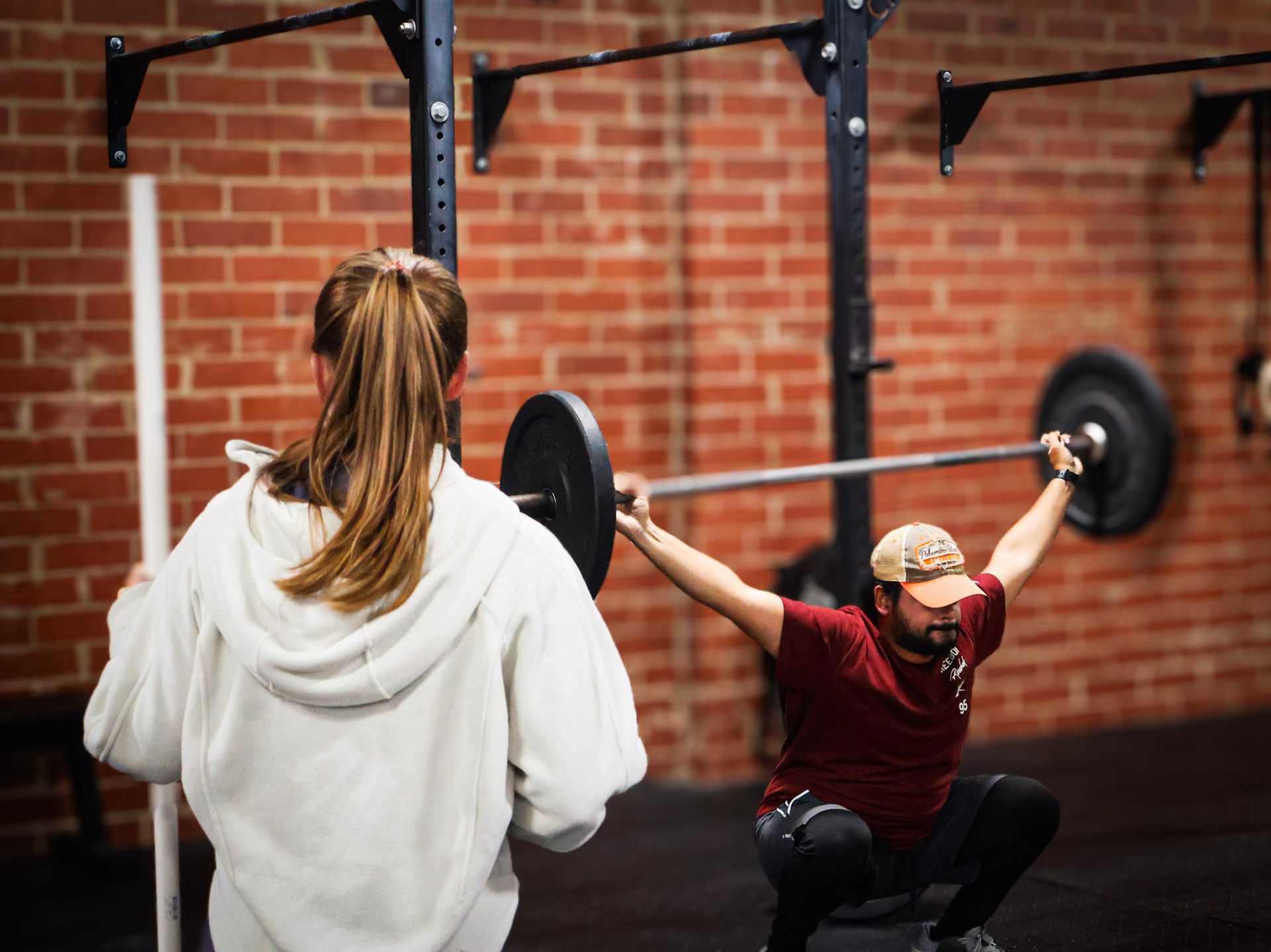 A man squatting with a bar over his head while a woman watches