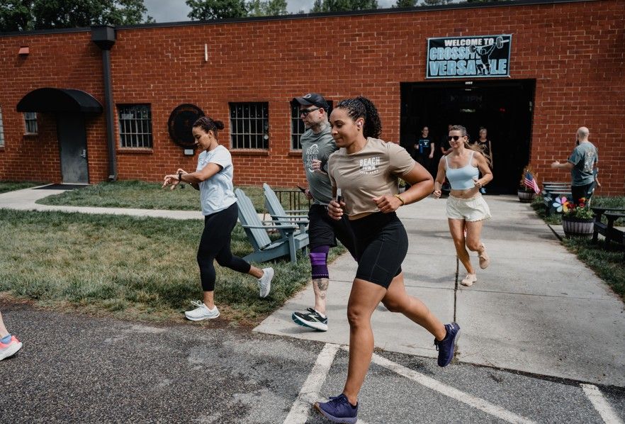 Runners in athletic gear jogging past a brick building on a paved path outdoors