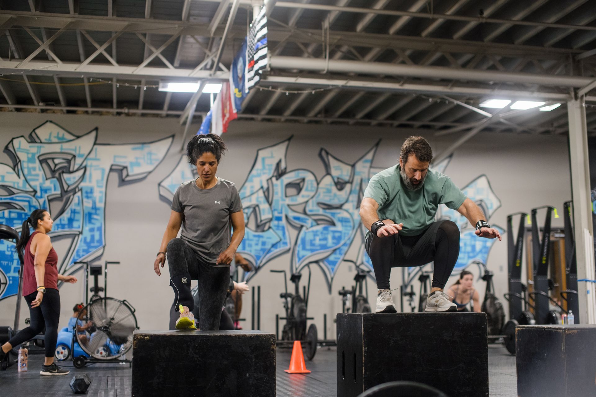 A group of people are squatting on boxes in a gym.