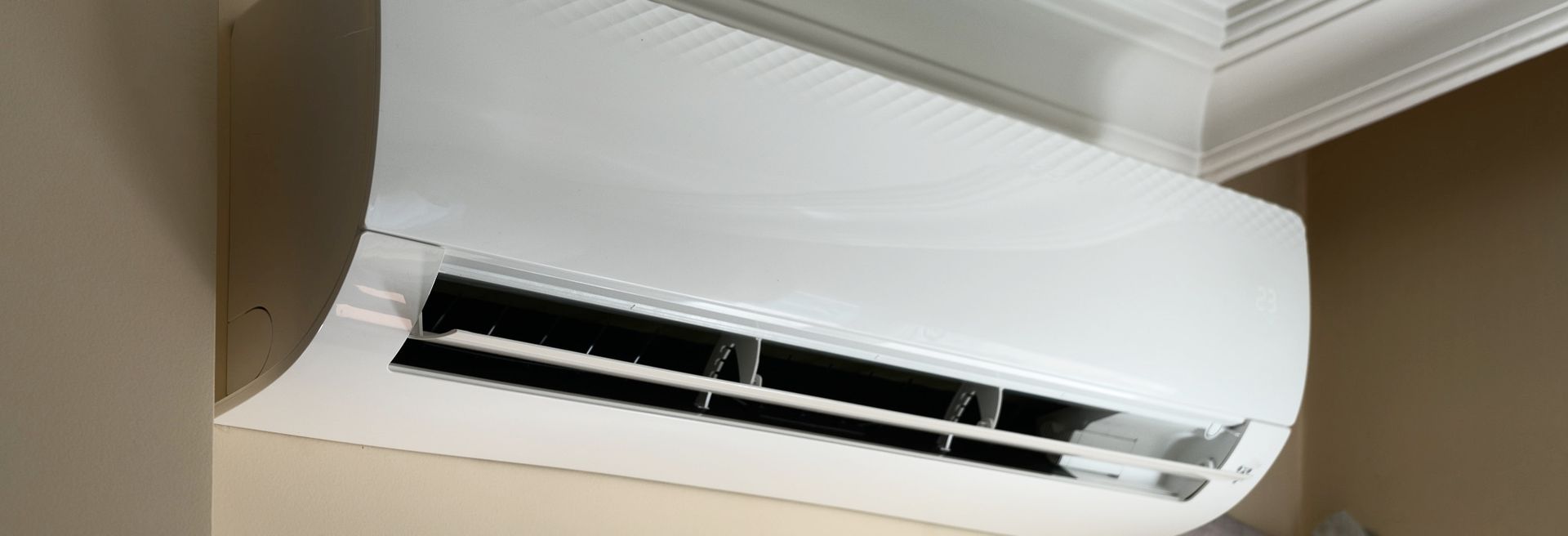 White wall-mounted air conditioner unit on a beige wall, viewed from below