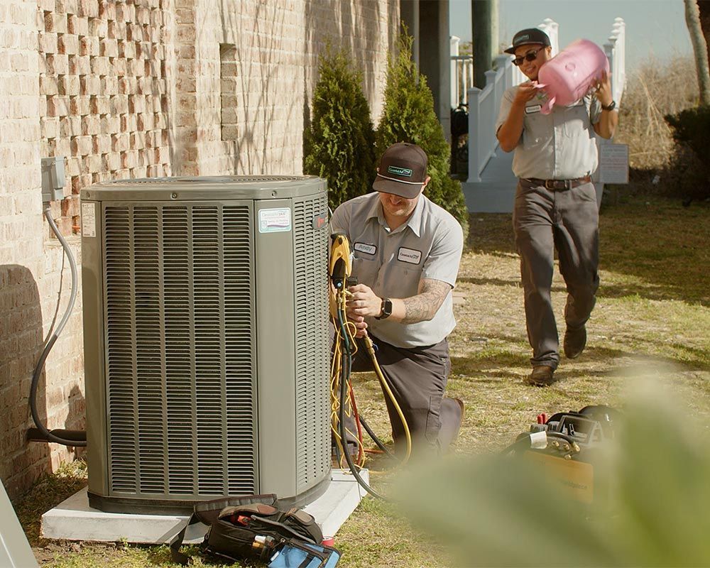 Two men are working on an air conditioner outside of a house