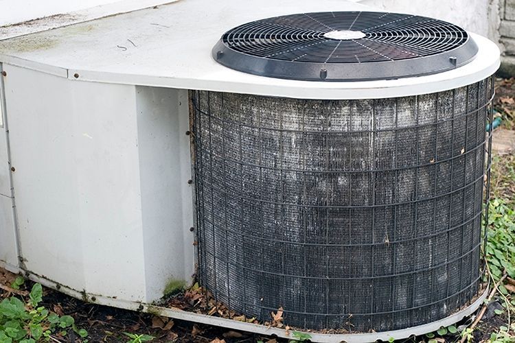 Outdoor air conditioning unit with a large fan on top, sitting beside a white building.