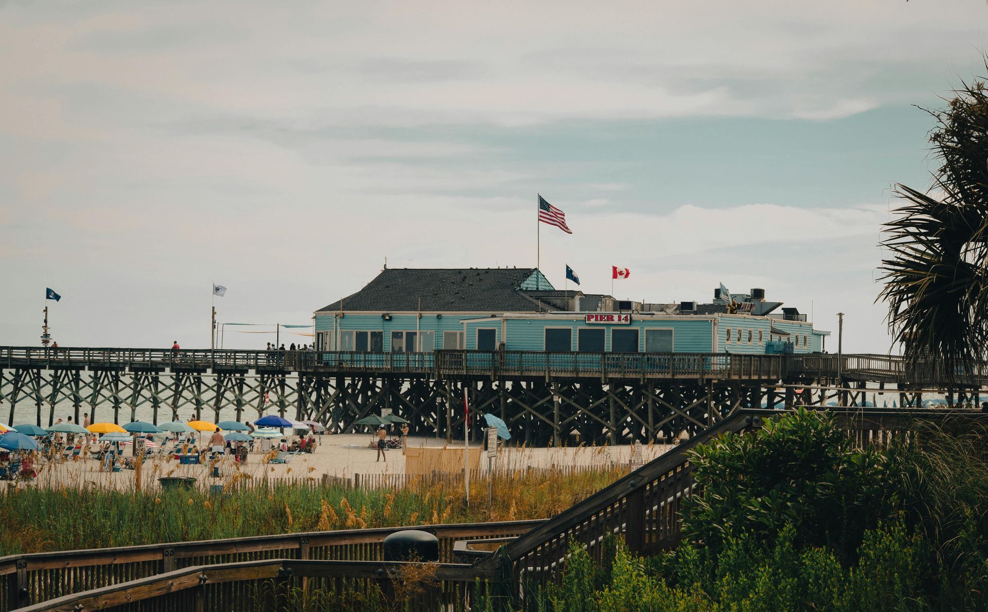 Beachfront pier with a building and flags overlooking sandy shore and ocean.