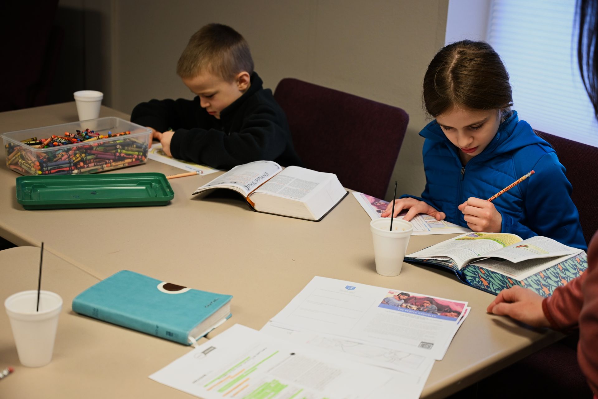 A boy and a girl are sitting at a table reading the Bible.