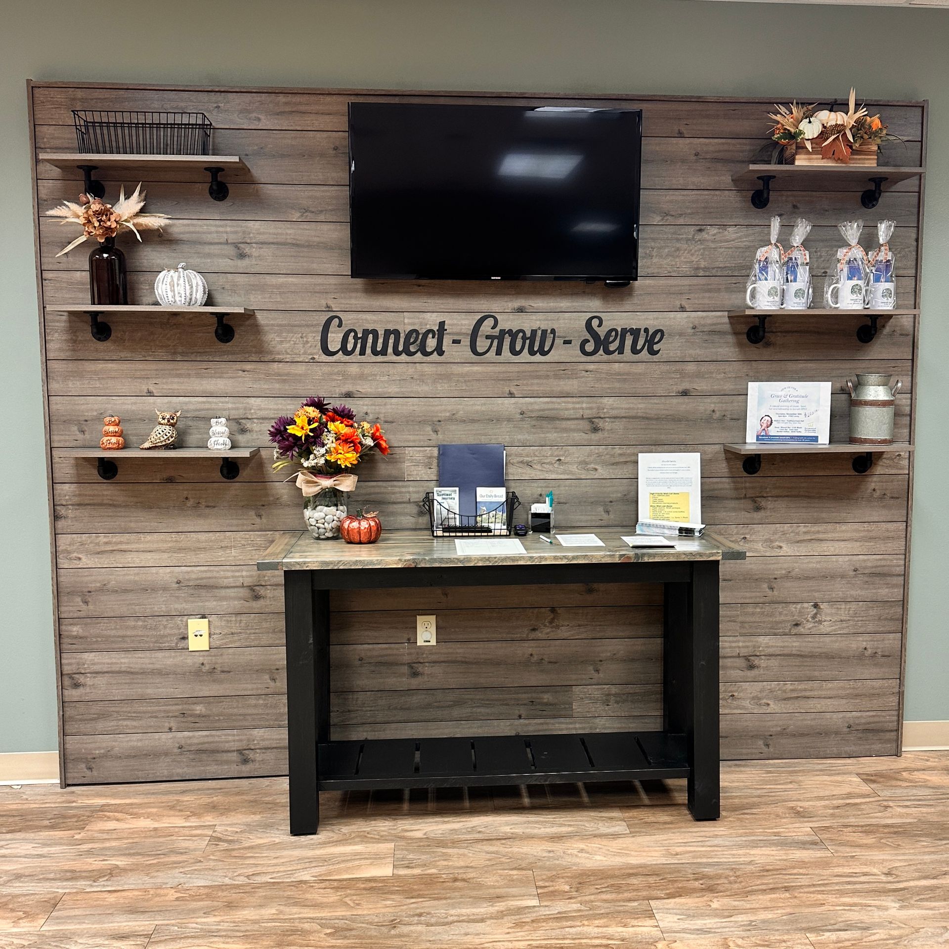 Reception area with rustic wood backdrop, shelves with decor, TV, and table with resources.