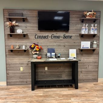 Reception area with rustic wood backdrop, shelves with decor, TV, and table with resources.