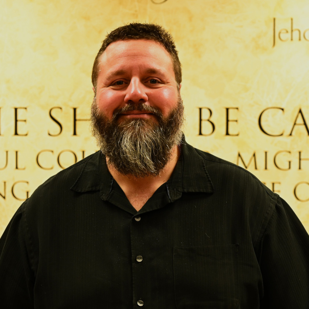 A man with a beard is smiling in front of a wall 