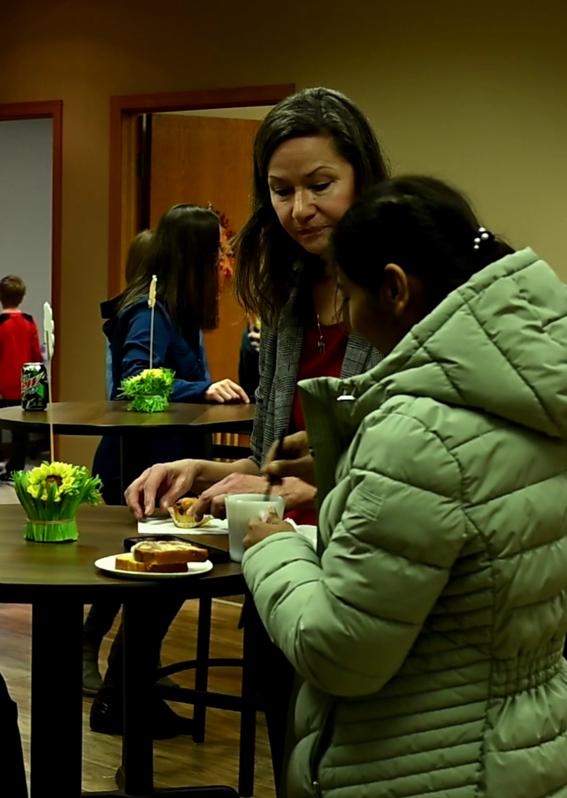 A woman in a green jacket is talking to another woman at a table
