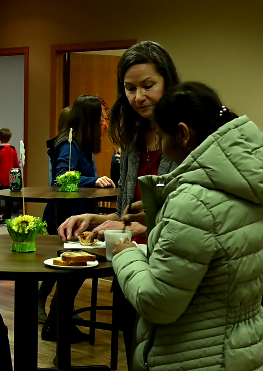 A woman in a green jacket is talking to another woman at a table