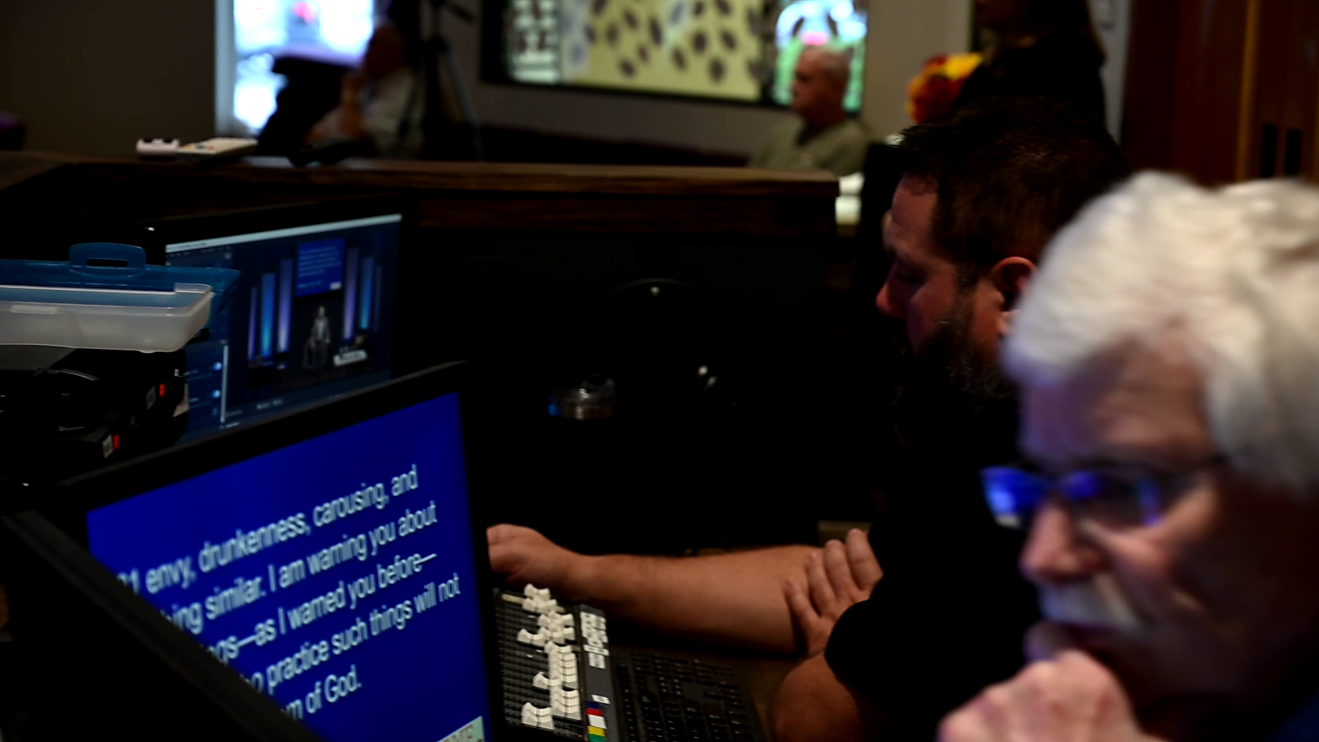 Two men are sitting in front of a computer screen that says ' i am sorry ' on it