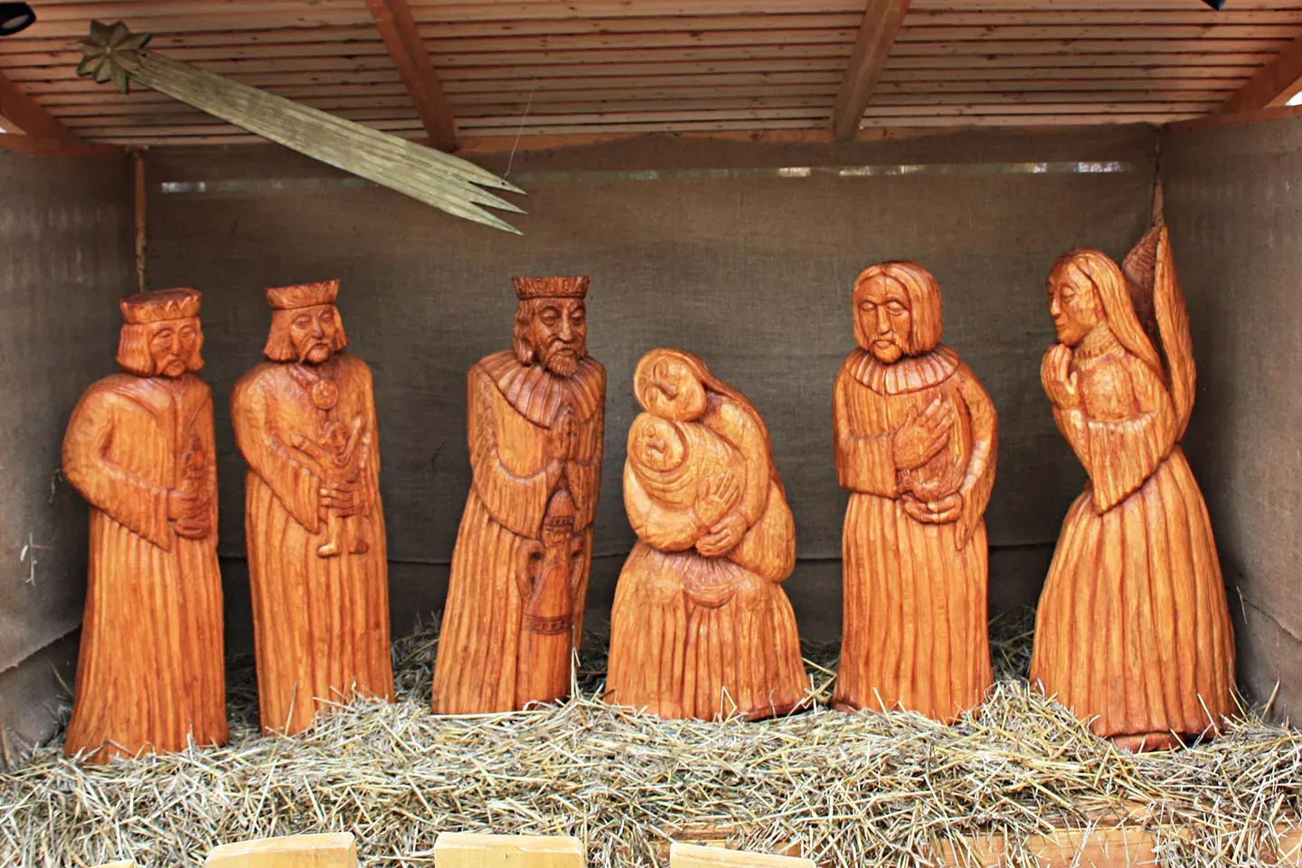 Wooden Nativity scene with figures, star, and hay in a sheltered structure.