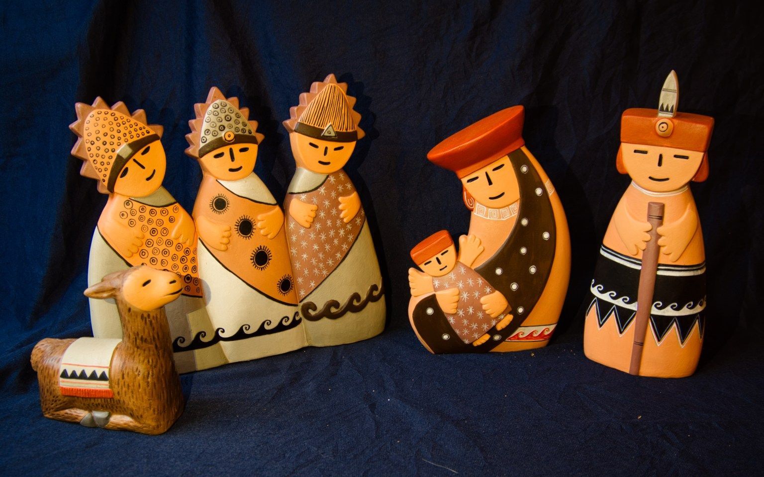 Hand-painted nativity set: figures with patterned clothing, llama, blue background.