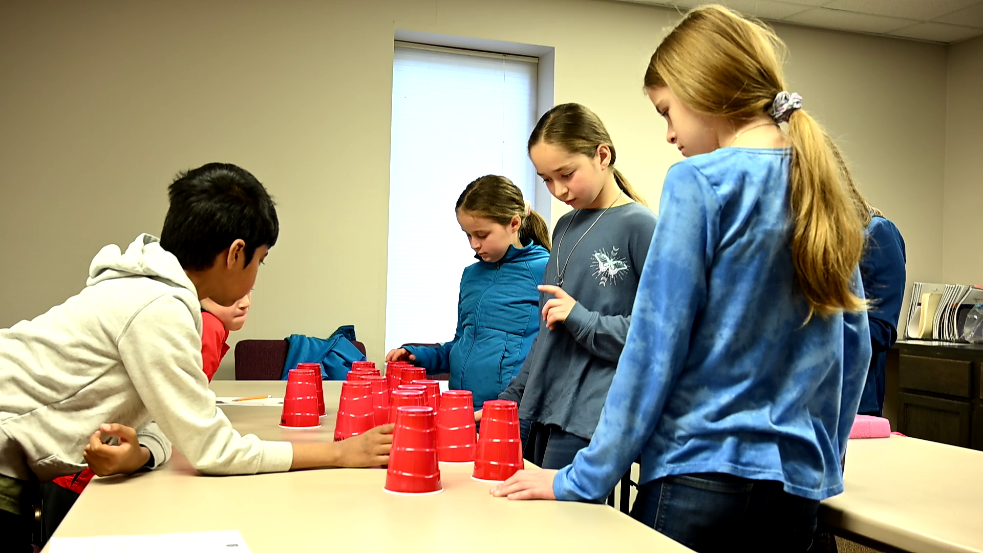 A group of children are playing a game with red cups on a table.