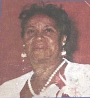 Woman with dark hair, wearing a white collared shirt and pearl necklace. She is wearing earrings and smiling slightly.