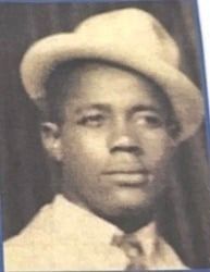 Man in a fedora and suit, looking towards the viewer.
