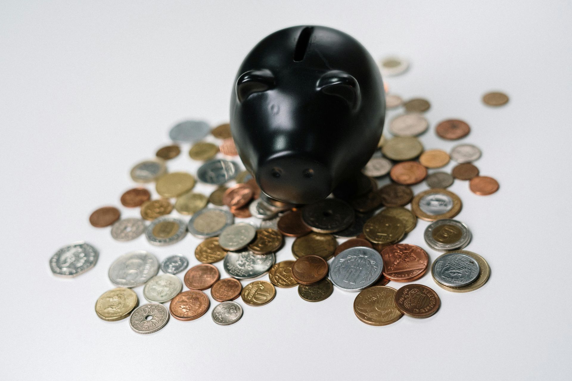 Black piggy bank surrounded by various coins on a white surface.