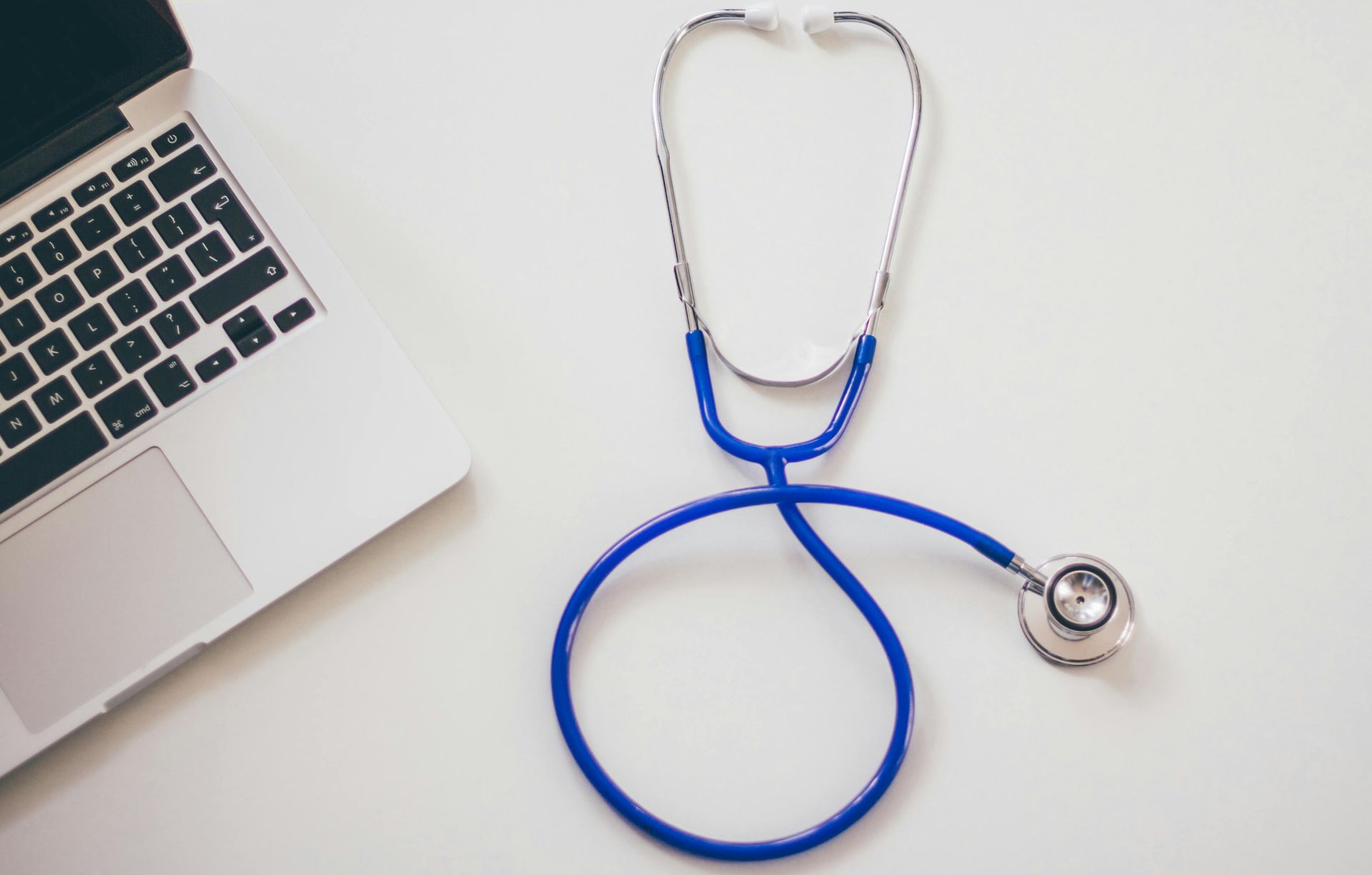Laptop next to blue stethoscope on white surface.