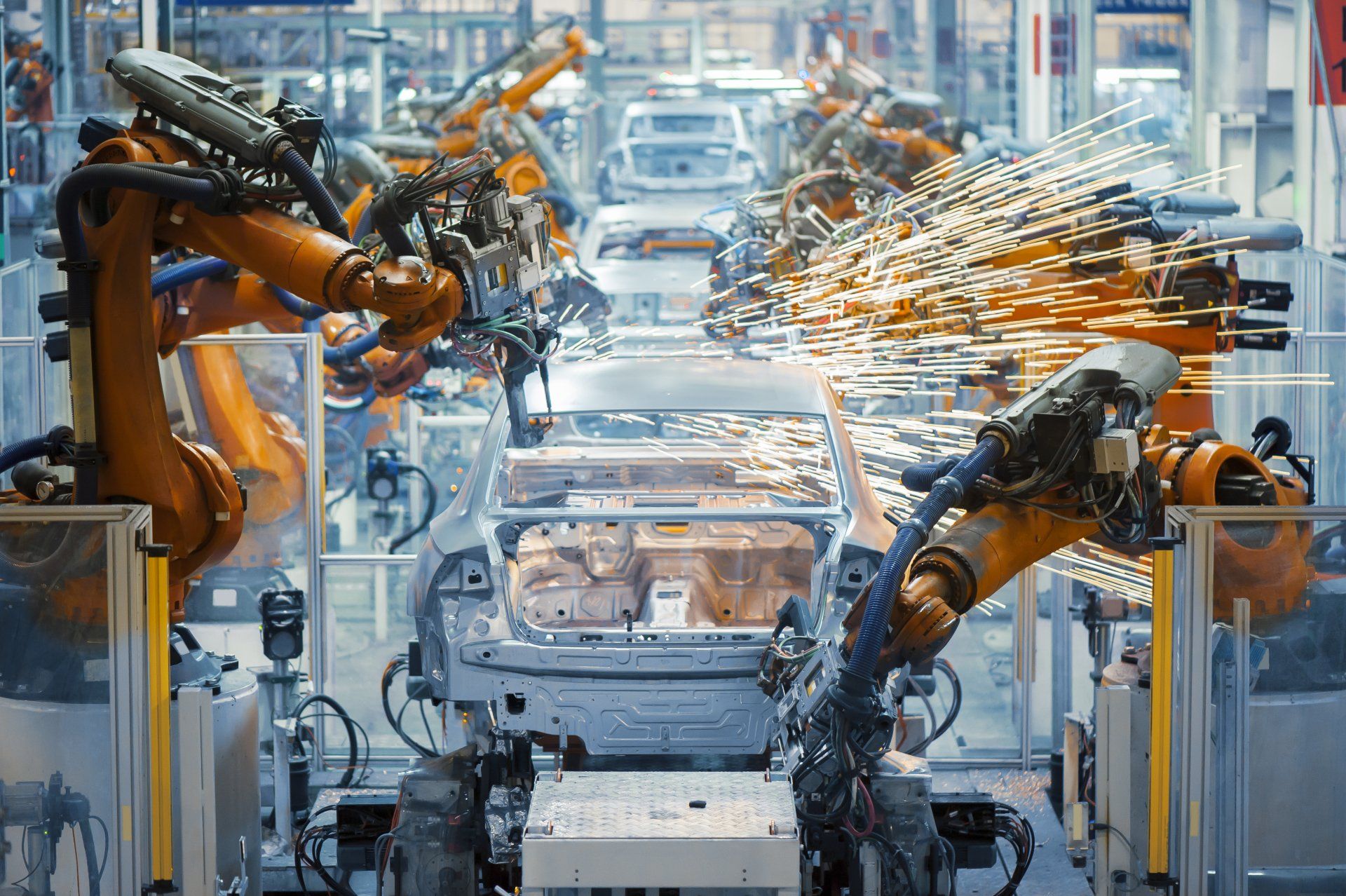 A row of robots are working on a car in a factory.