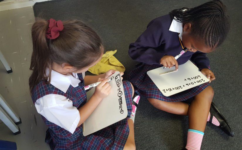 Two young girls are sitting on the floor writing on a piece of paper