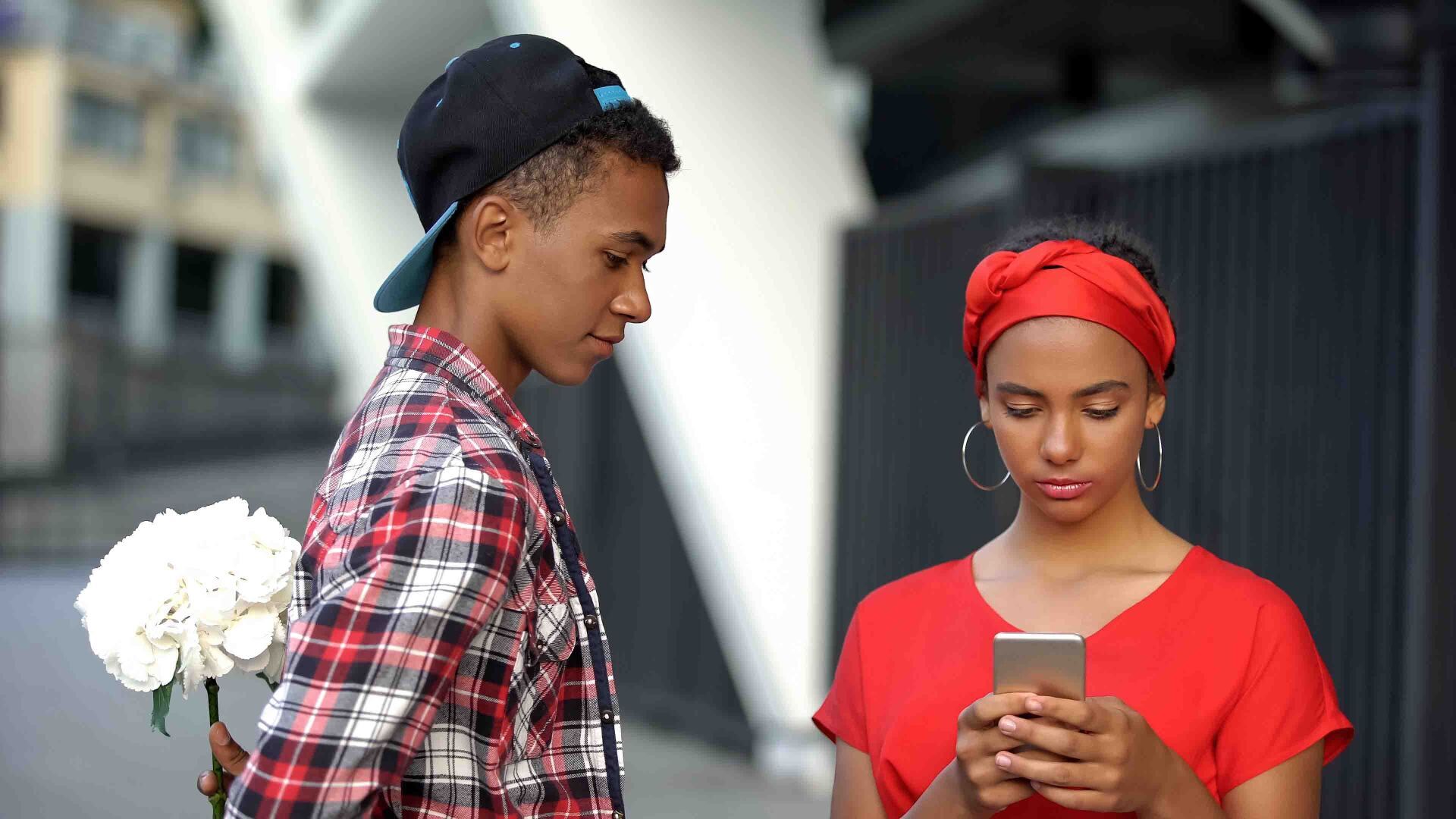 A man is holding a bouquet of flowers while a woman looks at her phone.