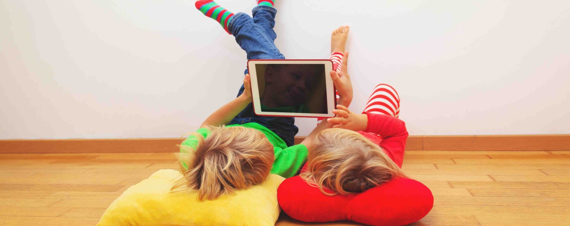Two children are laying on the floor using a tablet computer.