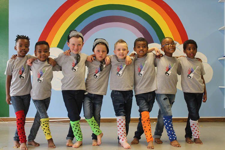 A group of children are posing for a picture in front of a rainbow.