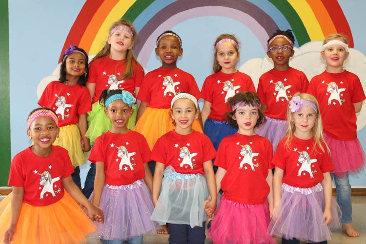 A group of young girls are posing for a picture in front of a rainbow.