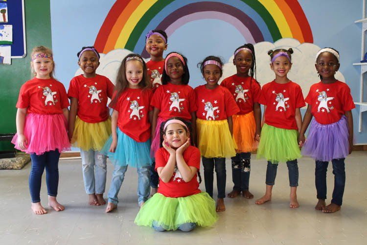A group of young girls are posing for a picture in front of a rainbow.